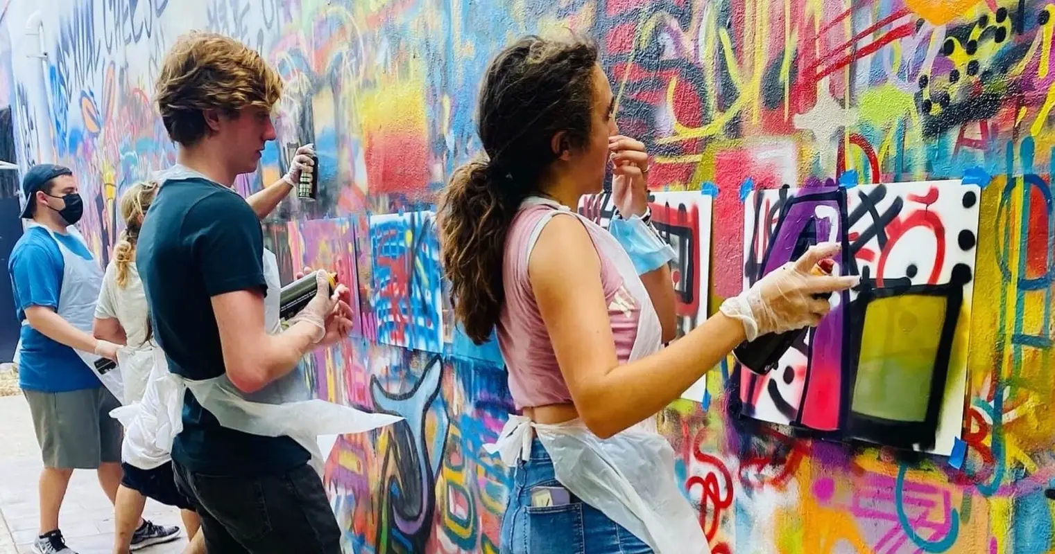 Participants in aprons and gloves spray-painting panels on a graffiti wall