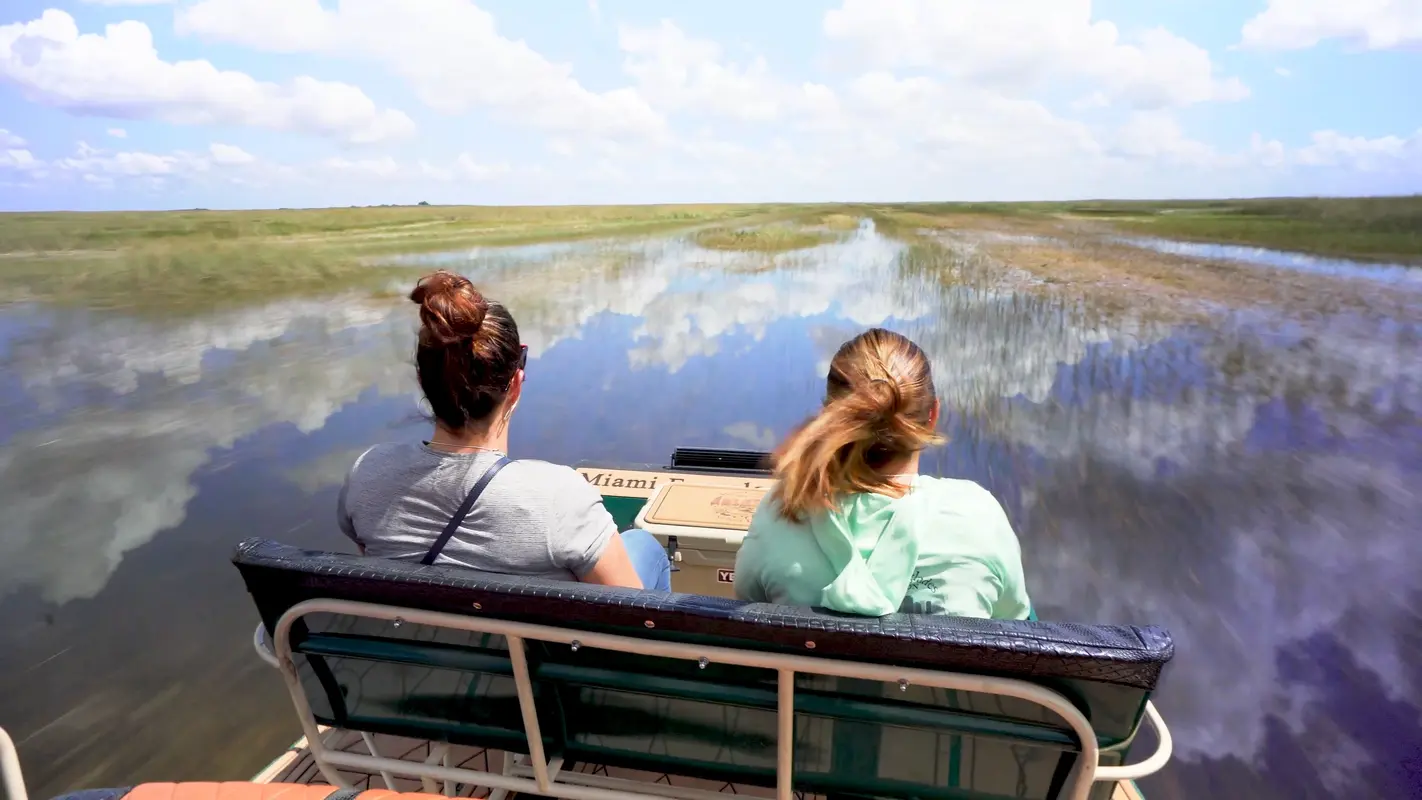 Two guests on an airboat bench gliding across Everglades sawgrass