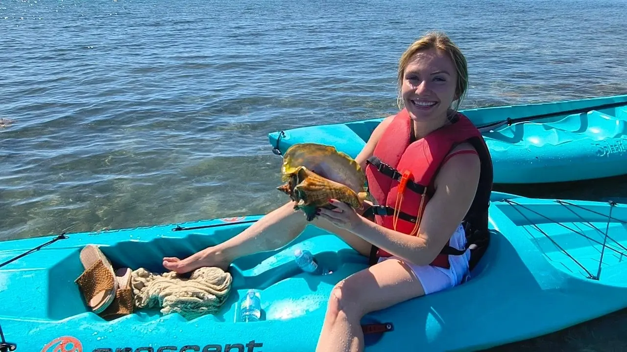 A smiling kayaker in a life vest holding a seashell