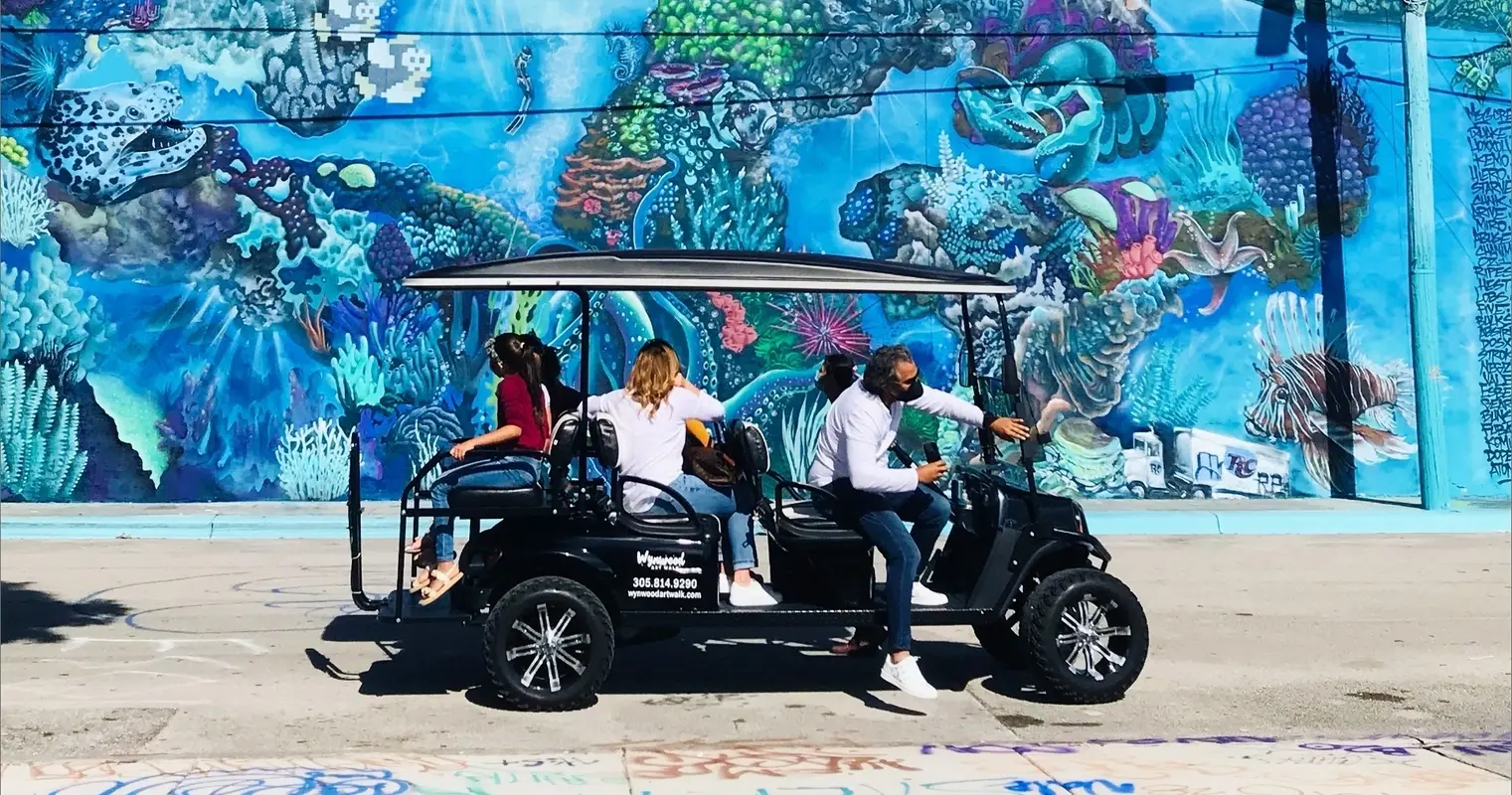 Guests in a black golf cart in front of an ocean-themed mural