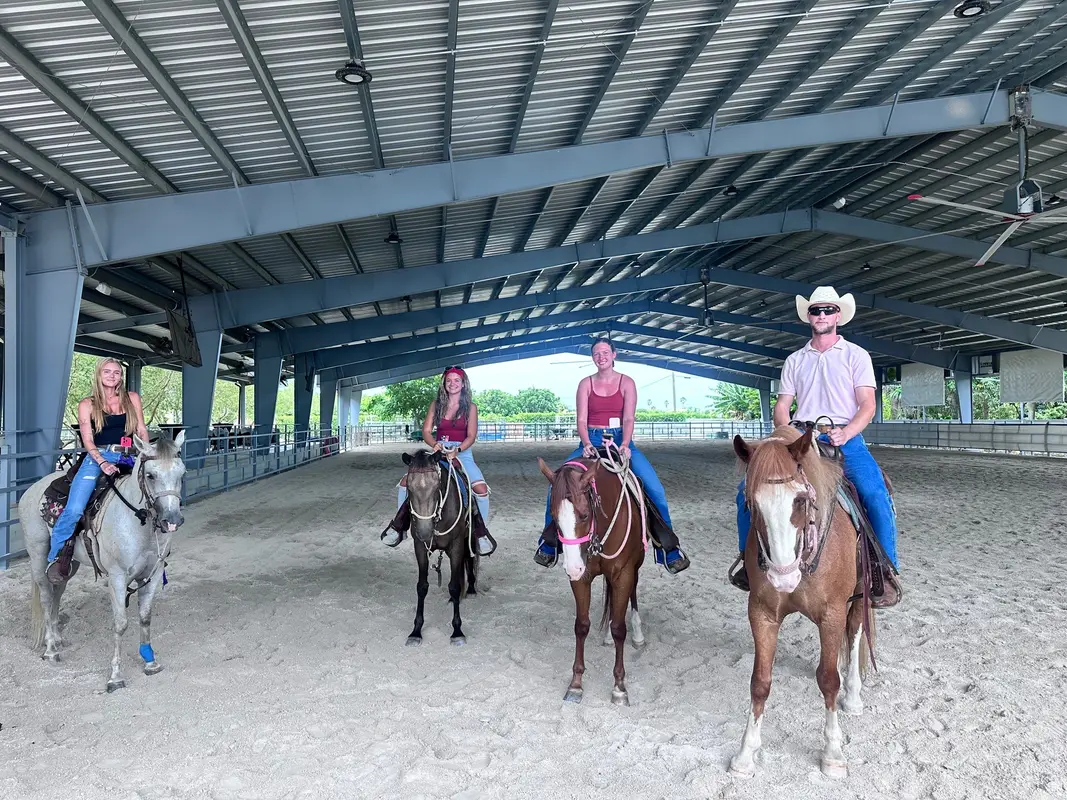Four riders on horseback inside a covered riding arena