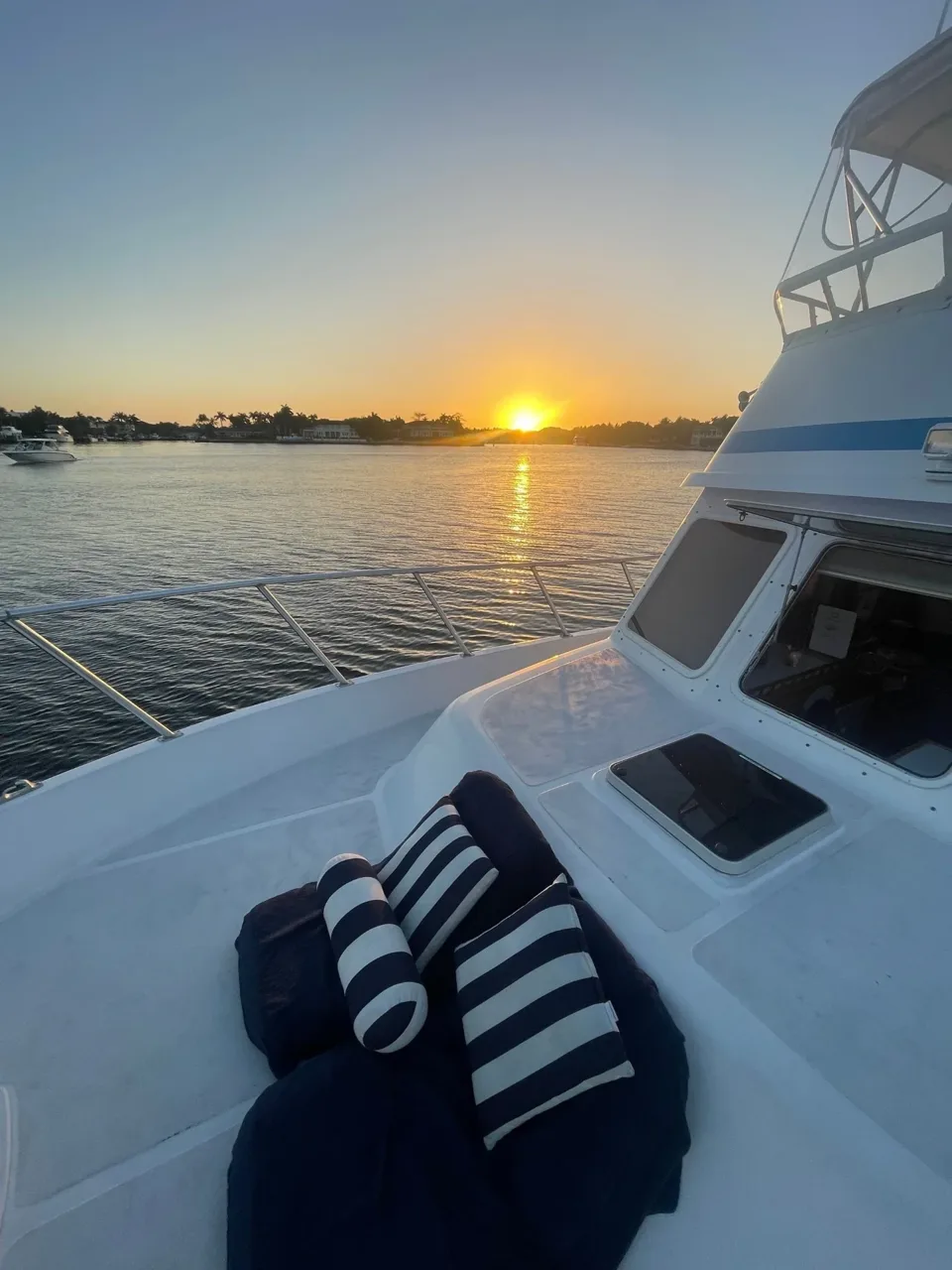 White yacht bow with striped cushions overlooking the water at sunset