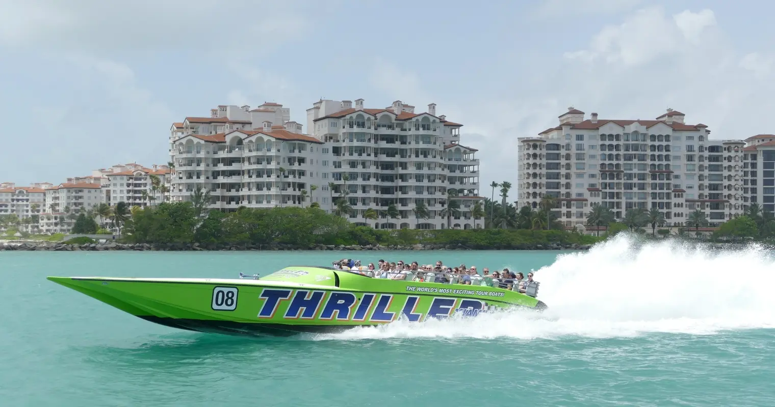 A green Thriller speedboat passing Fisher Island buildings