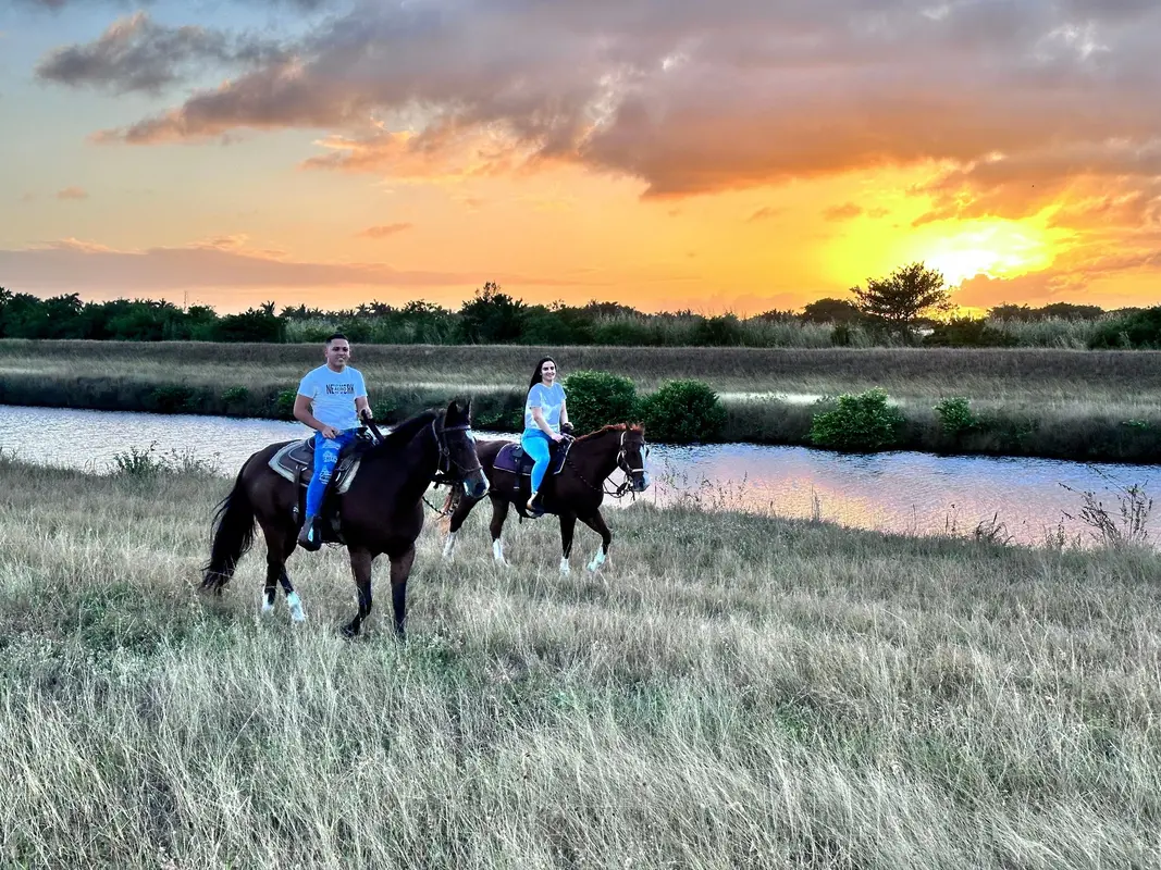Two riders on horseback beside a canal at sunset