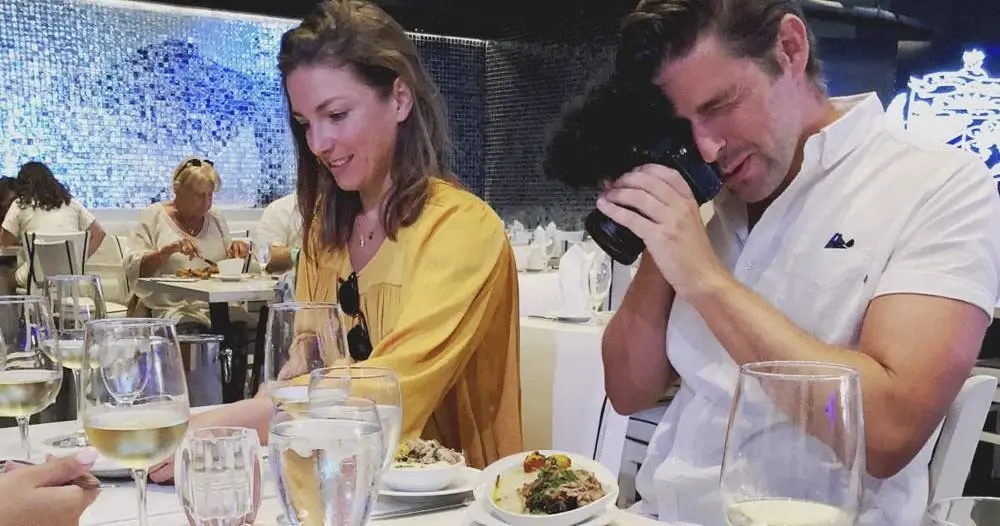Guests at a restaurant table, one filming with a camera