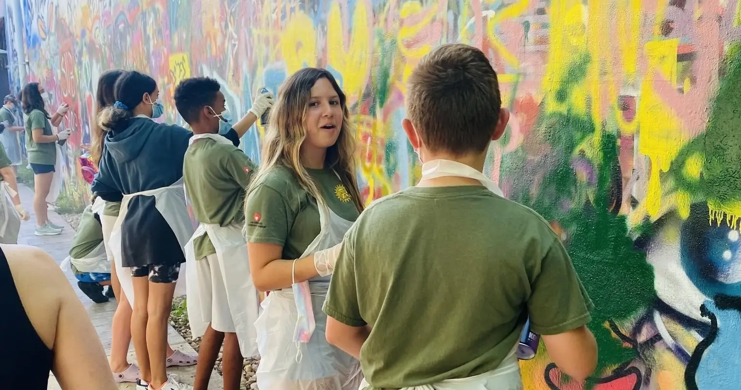 A group in aprons spray-painting along a graffiti wall