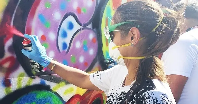 A participant in mask, goggles and gloves using a spray can