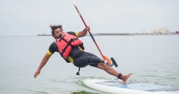 A paddler in a life vest losing balance on a paddle board