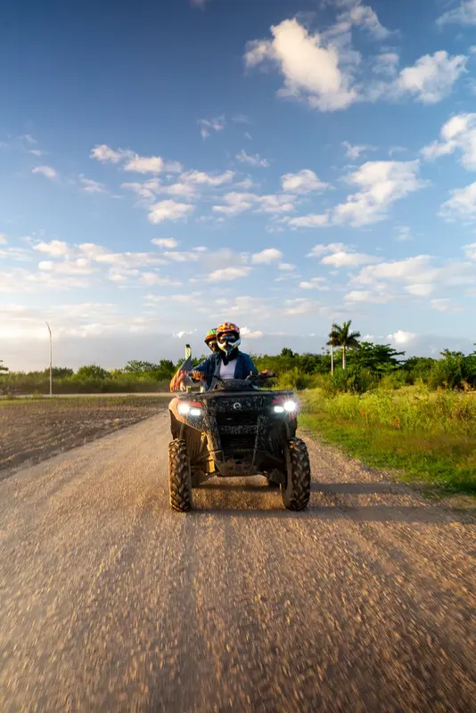 An ATV rider in a helmet on a dirt farm road under blue sky