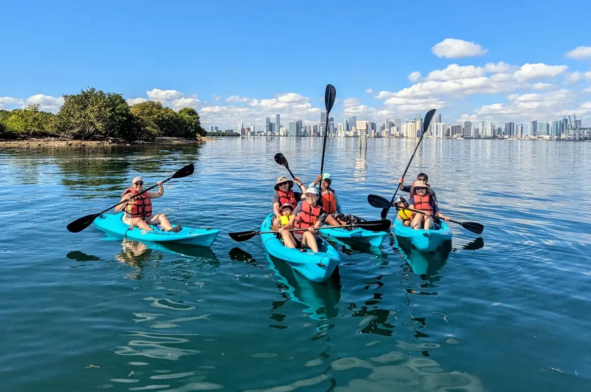 A group of kayakers raising paddles with the Miami skyline behind