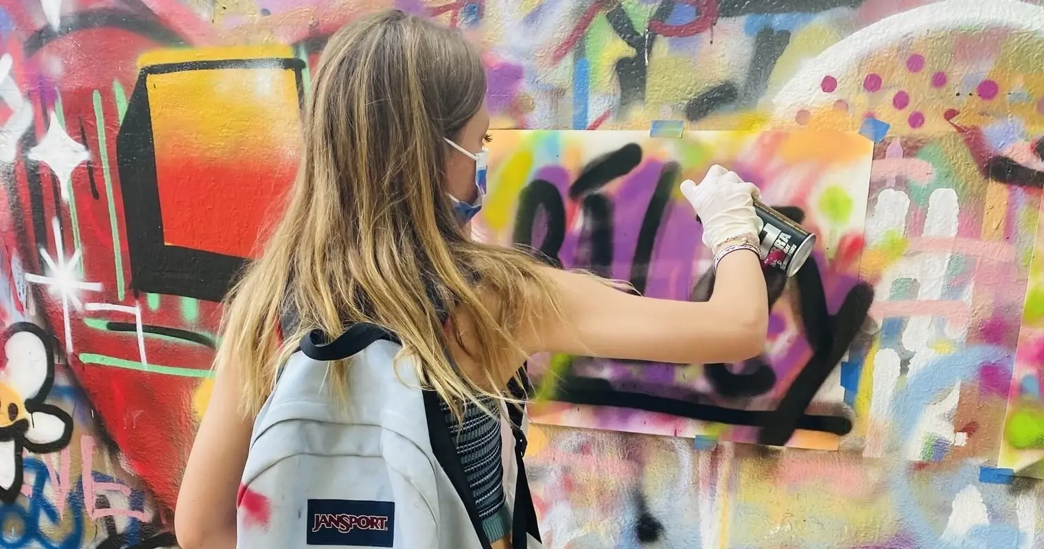 A participant spray-painting a large panel on a colorful wall