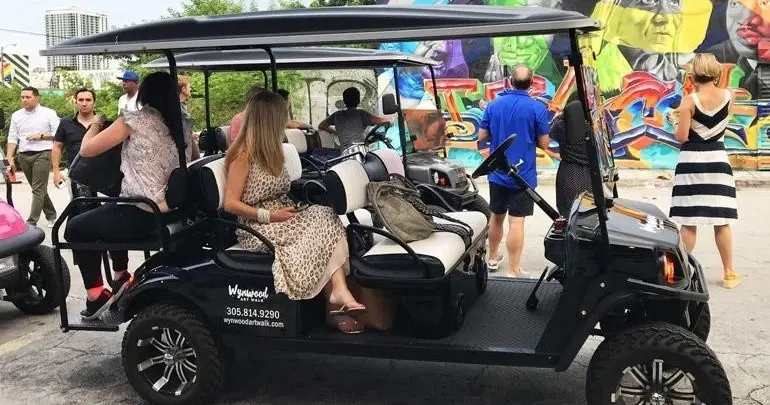 Guests in a golf cart near a colorful graffiti wall