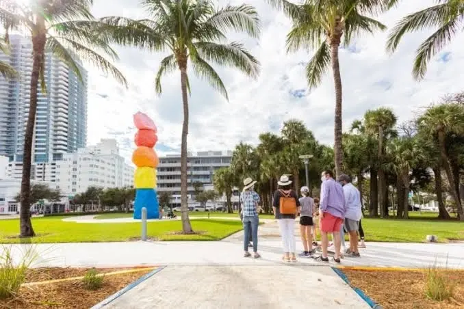 A walking group in Lummus Park beside a colorful stacked sculpture