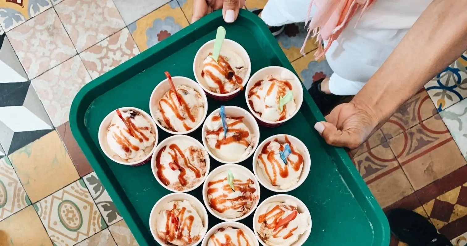 A tray of ice cream cups drizzled with sauce over a patterned tile floor