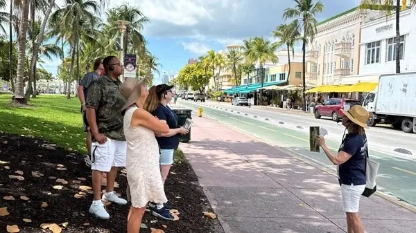A guide showing a photo to a group on an Ocean Drive sidewalk