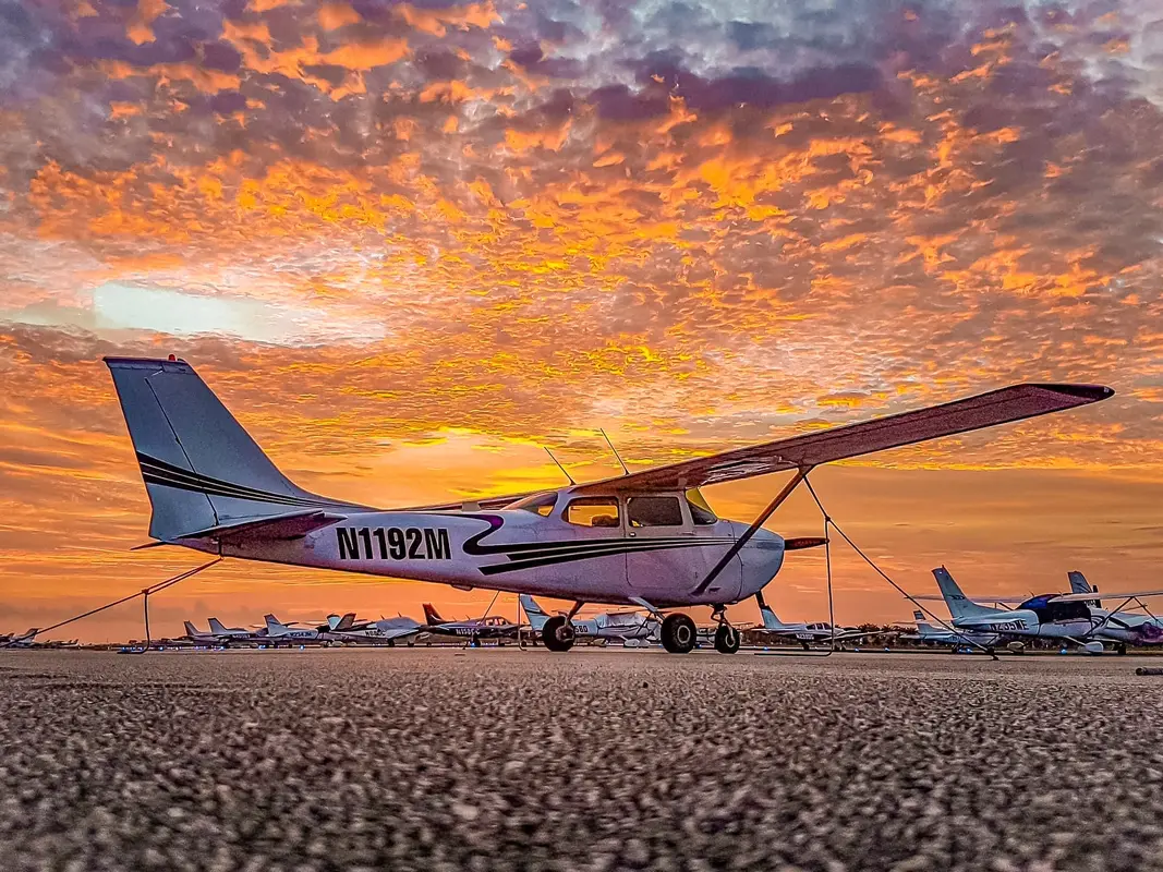 A Cessna 172 on the tarmac under an orange sunset sky