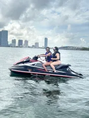 Two riders on a jet ski with the Miami skyline in the distance