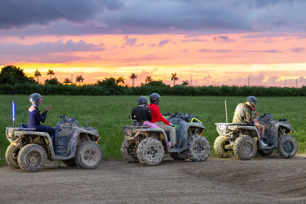 ATV riders beside a field at sunset