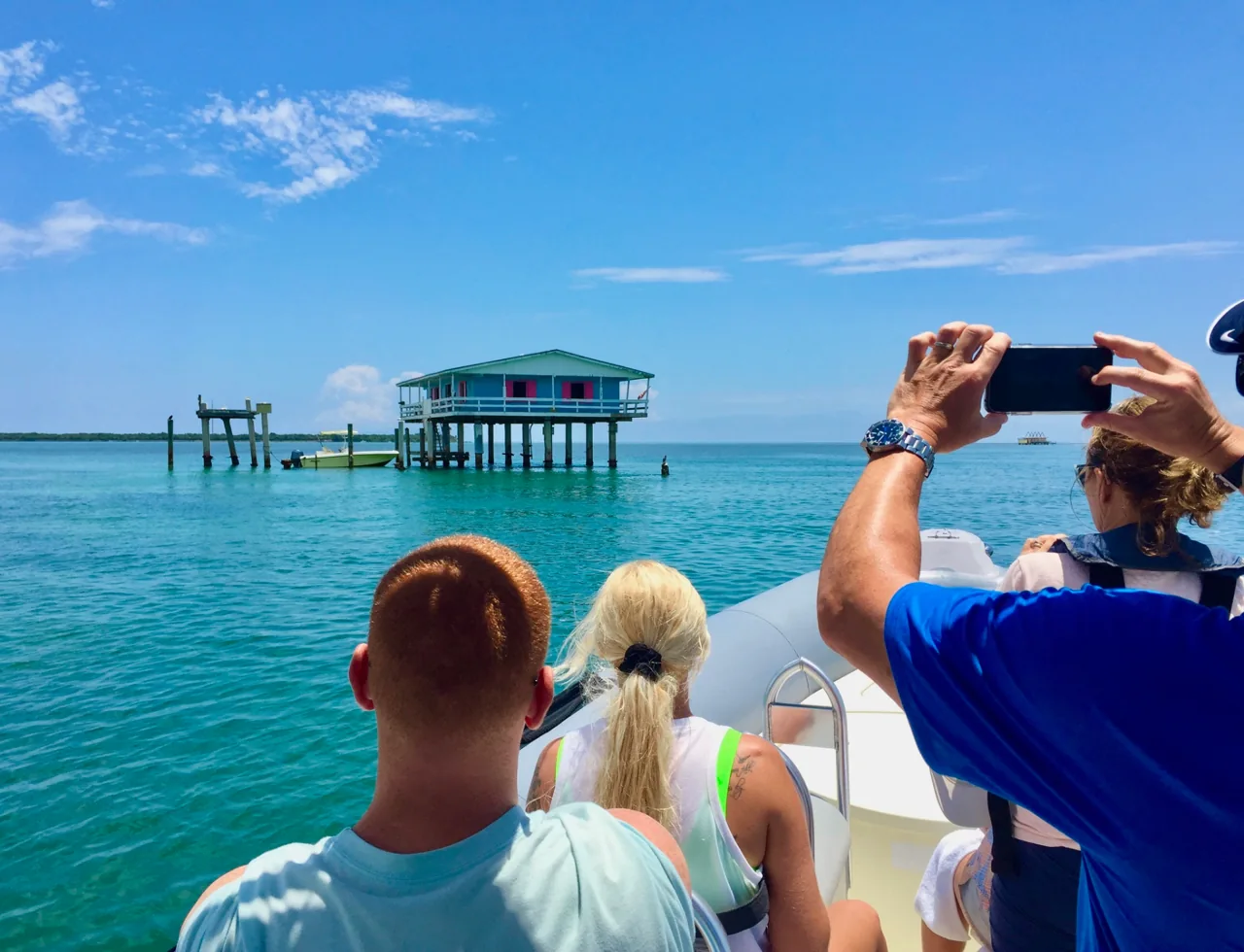 Passengers looking toward stilt houses across turquoise water
