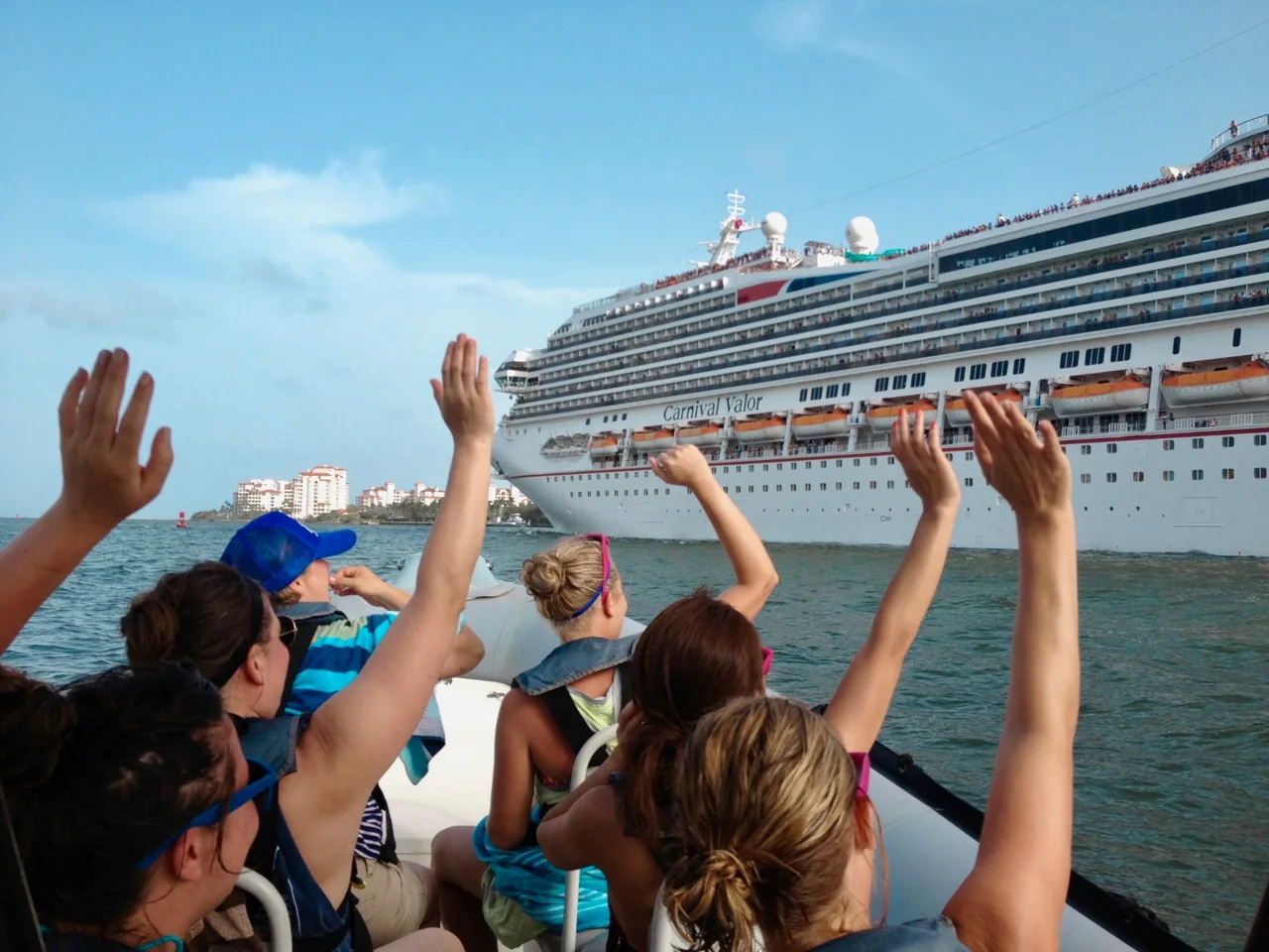 Passengers waving from a boat beside a cruise ship