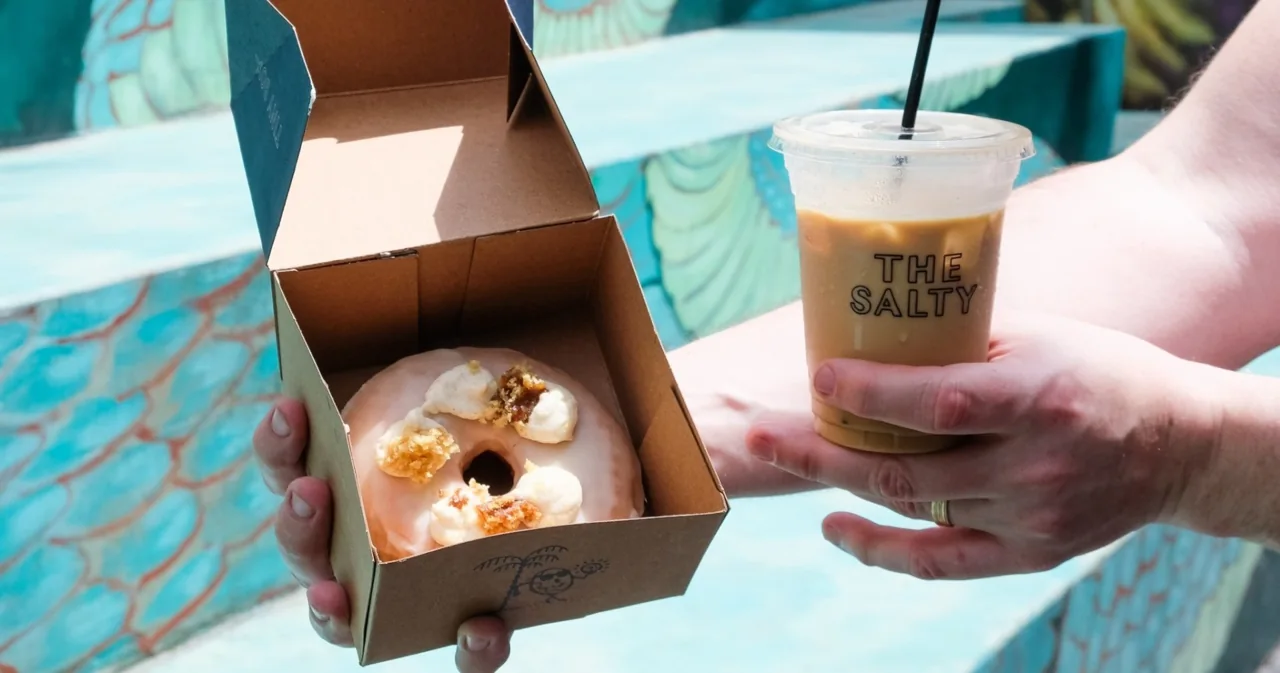 A donut box and iced drink held outside a café