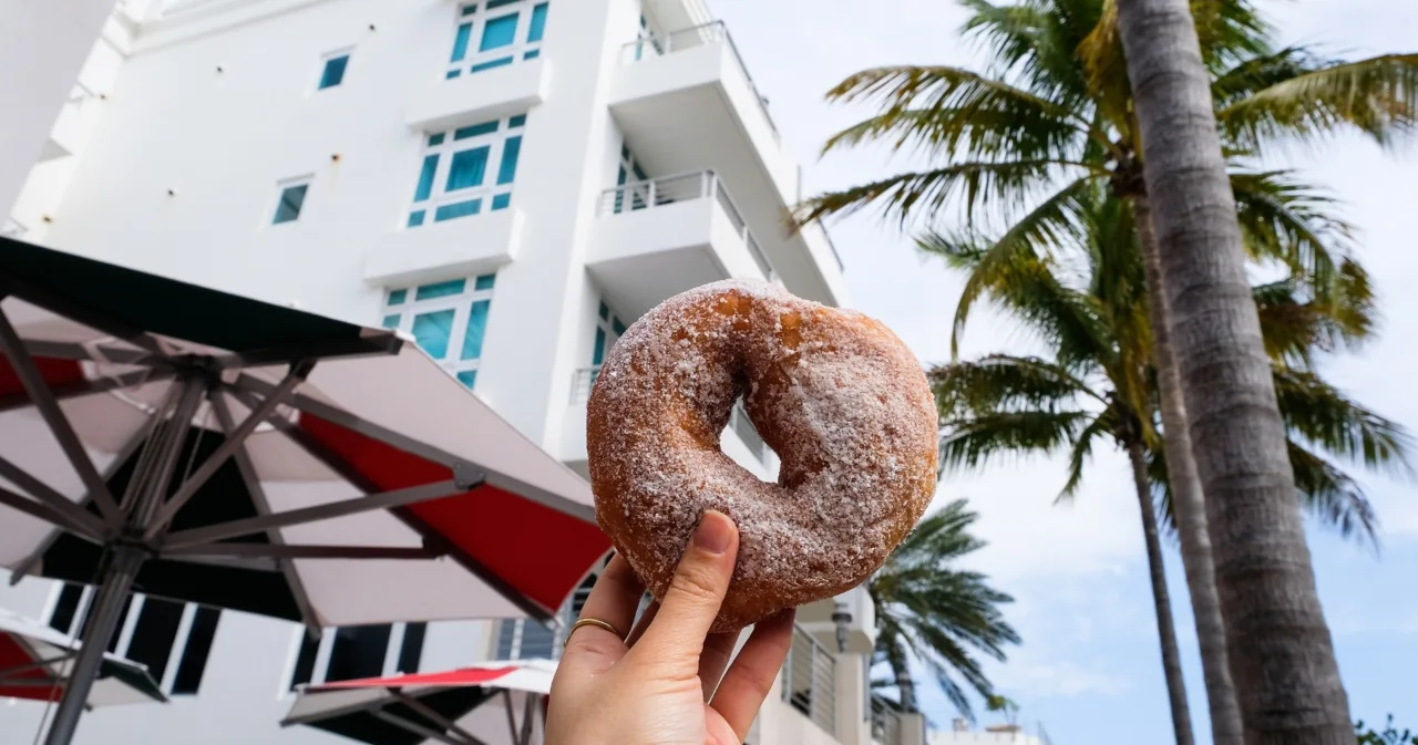 A visitor eating a donut outside a white building
