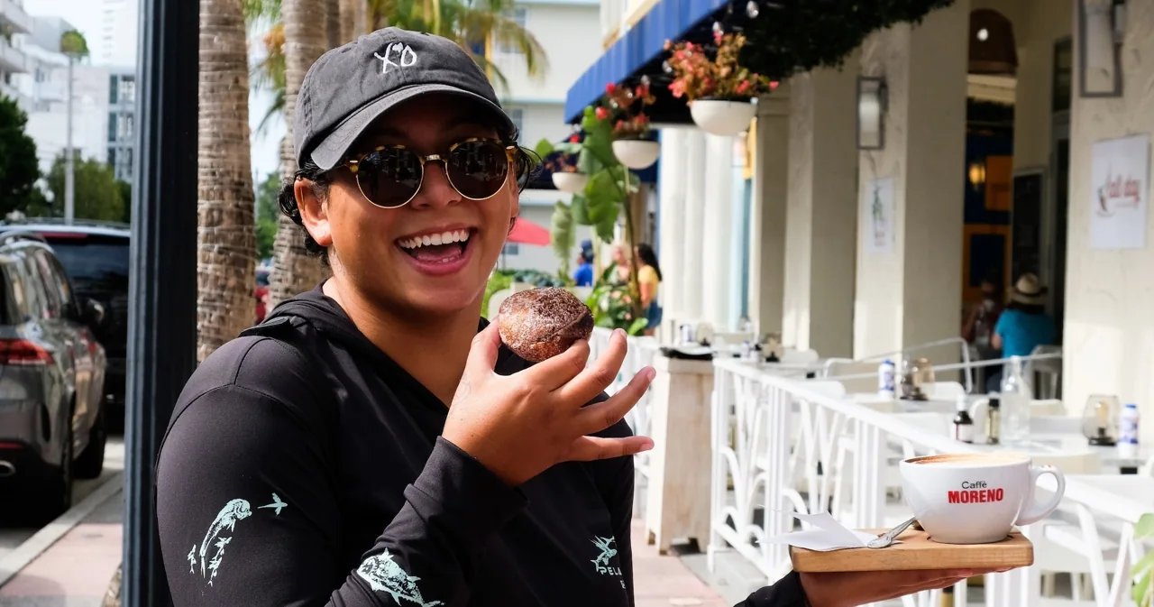 A visitor holding a donut on a shaded sidewalk