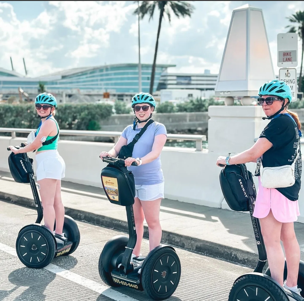 Three Segway riders on a waterfront path beneath palm trees