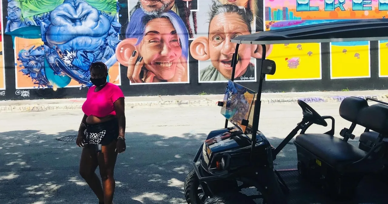 Visitors posing beside golf carts and a painted wall