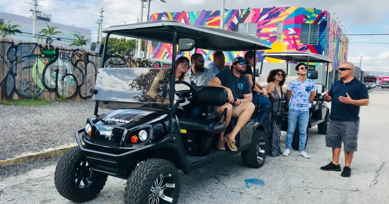 A golf cart and visitors beside a colorful street-art wall