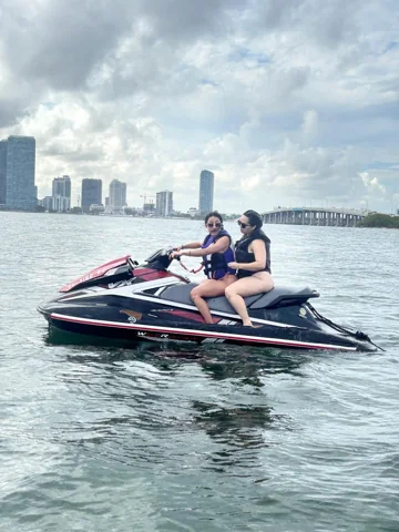 Two riders on a jet ski with the Miami skyline in the distance