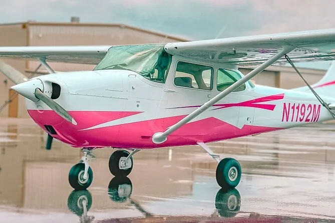 Pink-and-white propeller airplane parked beneath a hangar roof